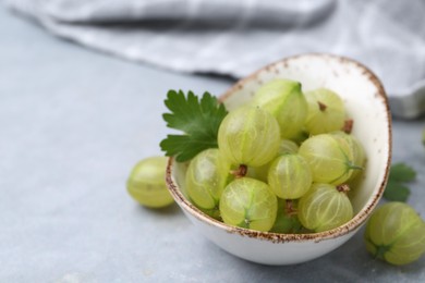 Photo of Fresh green gooseberries in bowl on grey table, closeup. Space for text