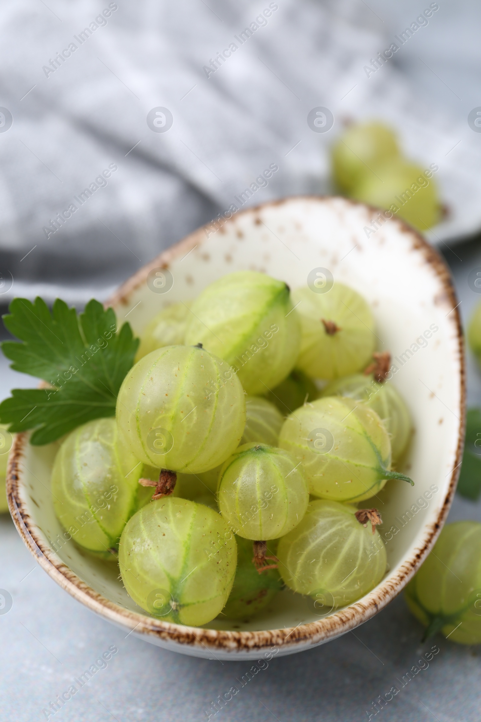 Fresh green gooseberries in bowl on grey table, closeup Photo of Fresh green gooseberries in bowl on grey table, closeup