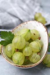 Photo of Fresh green gooseberries in bowl on grey table, closeup