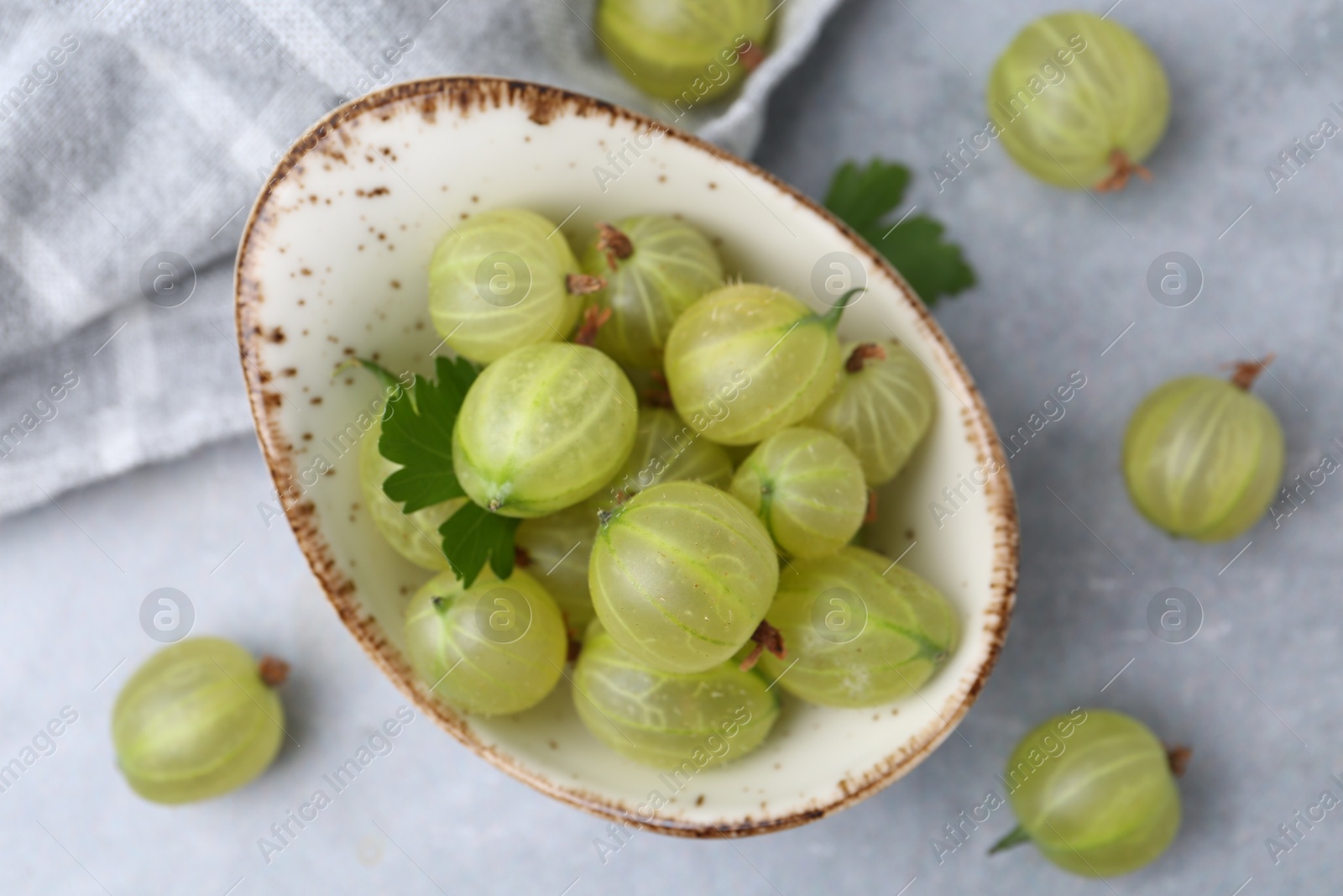 Photo of Fresh green gooseberries in bowl on grey table, closeup