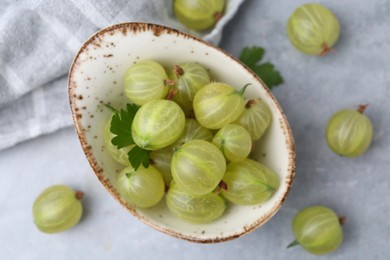 Photo of Fresh green gooseberries in bowl on grey table, closeup