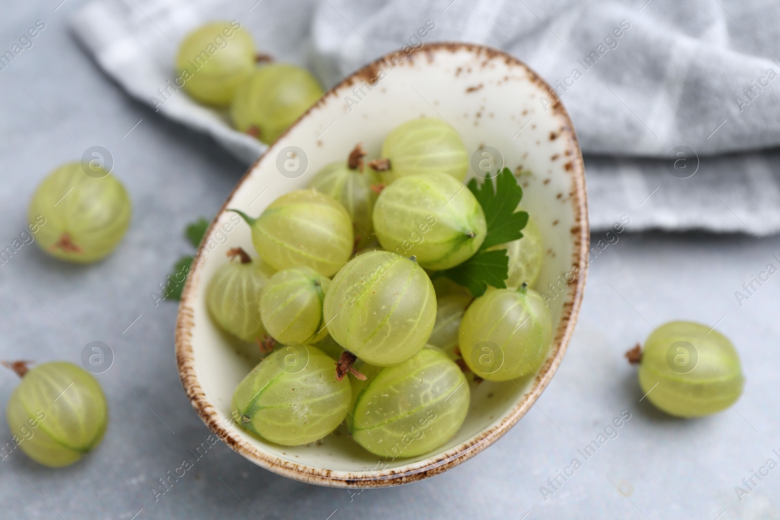 Fresh green gooseberries in bowl on grey table, closeup Photo of Fresh green gooseberries in bowl on grey table, closeup