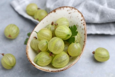 Photo of Fresh green gooseberries in bowl on grey table, closeup
