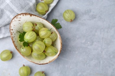 Photo of Fresh green gooseberries in bowl on grey table, top view. Space for text