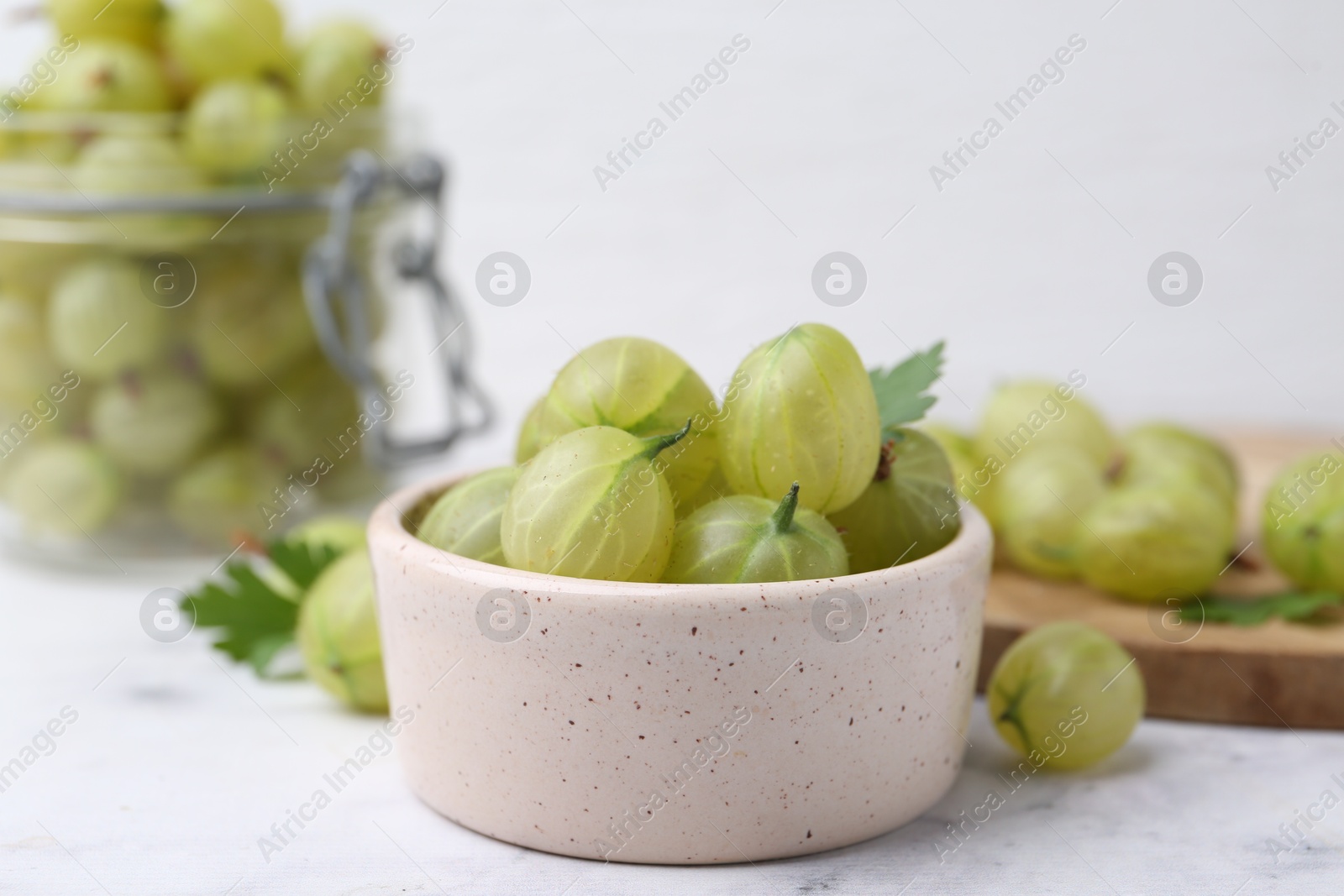 Photo of Fresh green gooseberries in bowl on white table, closeup