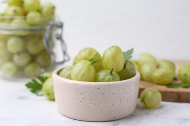 Photo of Fresh green gooseberries in bowl on white table, closeup
