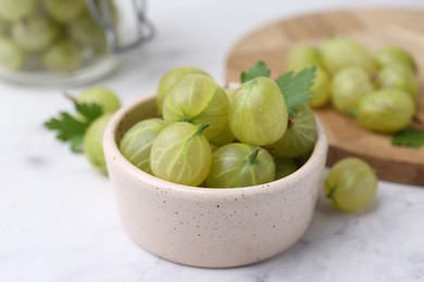 Photo of Fresh green gooseberries in bowl on white table, closeup