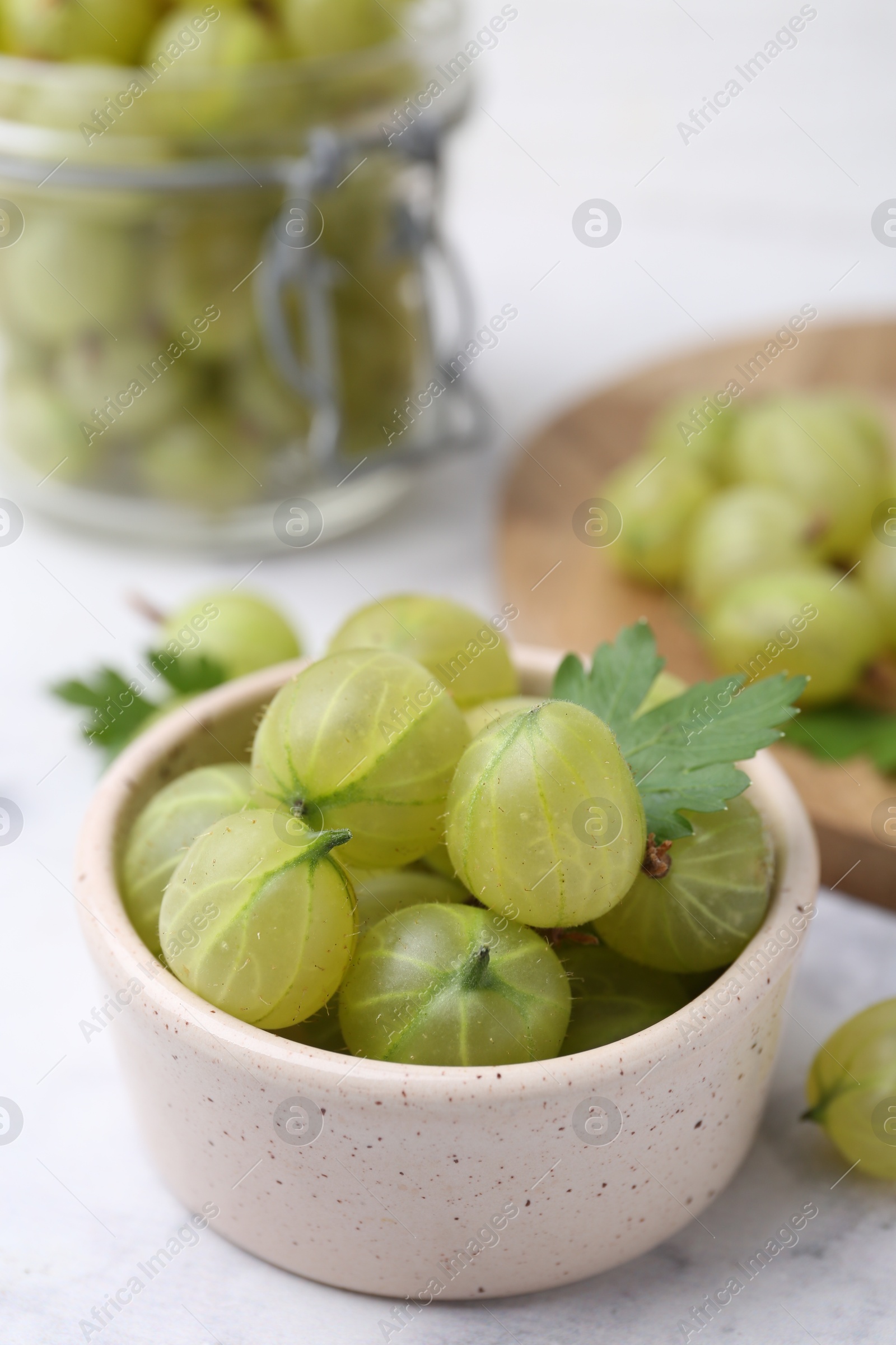 Photo of Fresh green gooseberries in bowl on white table, closeup