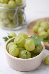 Photo of Fresh green gooseberries in bowl on white table, closeup
