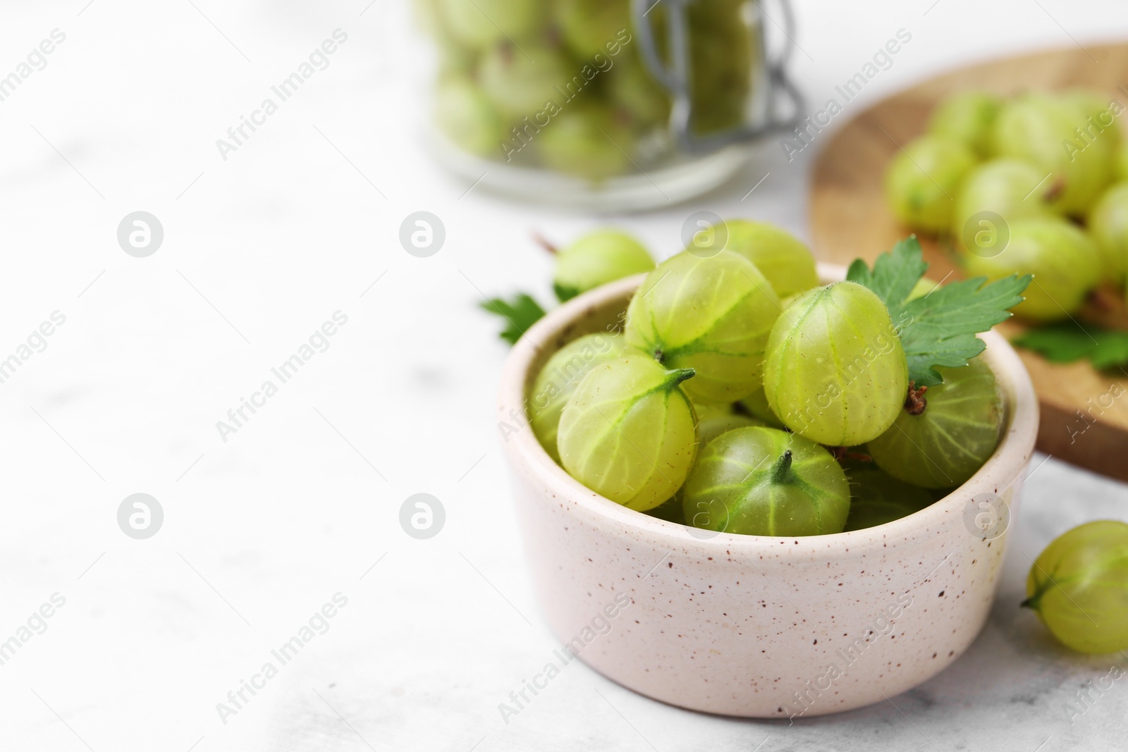 Photo of Fresh green gooseberries in bowl on white table, closeup. Space for text