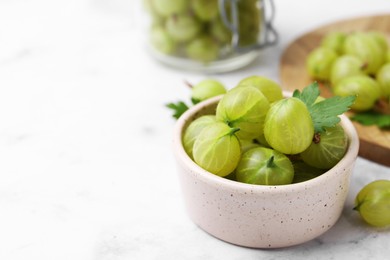 Photo of Fresh green gooseberries in bowl on white table, closeup. Space for text
