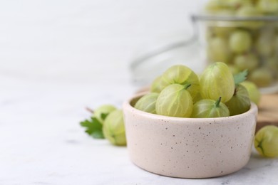 Photo of Fresh green gooseberries in bowl on white table, closeup. Space for text
