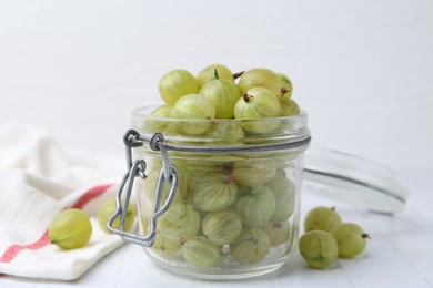 Photo of Fresh green gooseberries in jar on white table, closeup
