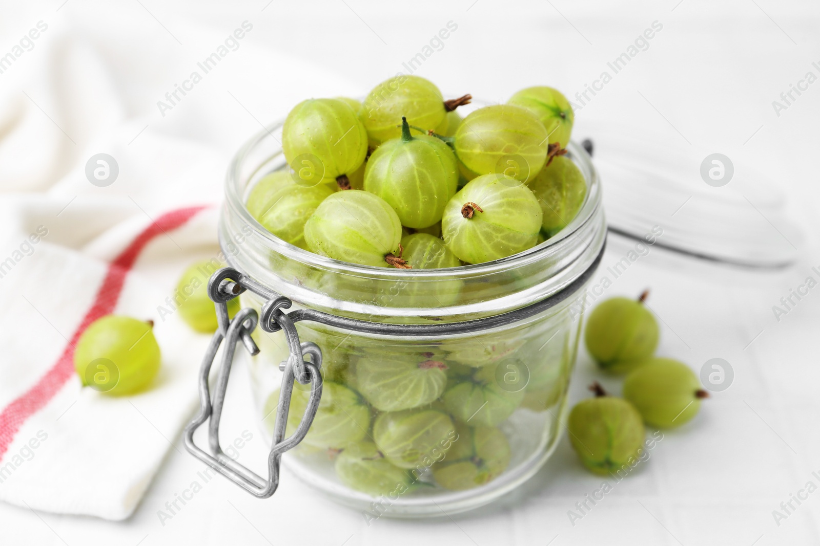 Fresh green gooseberries in jar on white table, closeup Photo of Fresh green gooseberries in jar on white table, closeup