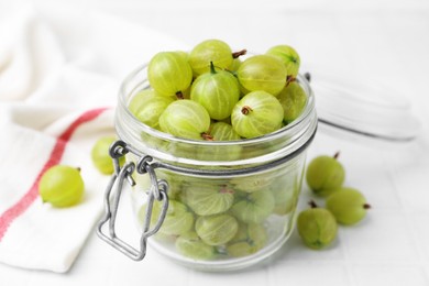 Photo of Fresh green gooseberries in jar on white table, closeup