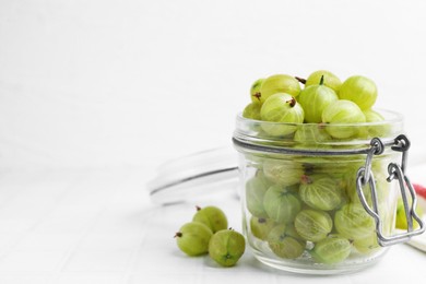 Photo of Fresh green gooseberries in jar on white table, closeup. Space for text