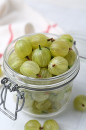 Photo of Fresh green gooseberries in jar on white table, closeup