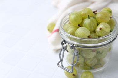 Photo of Fresh green gooseberries in jar on white table, closeup. Space for text