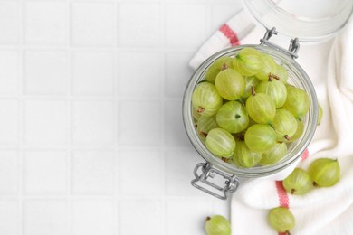 Photo of Fresh green gooseberries in jar on white tiled table, top view. Space for text