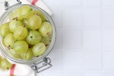Photo of Fresh green gooseberries in jar on white tiled table, top view. Space for text