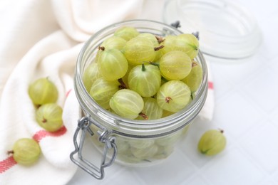 Photo of Fresh green gooseberries in jar on white table, closeup