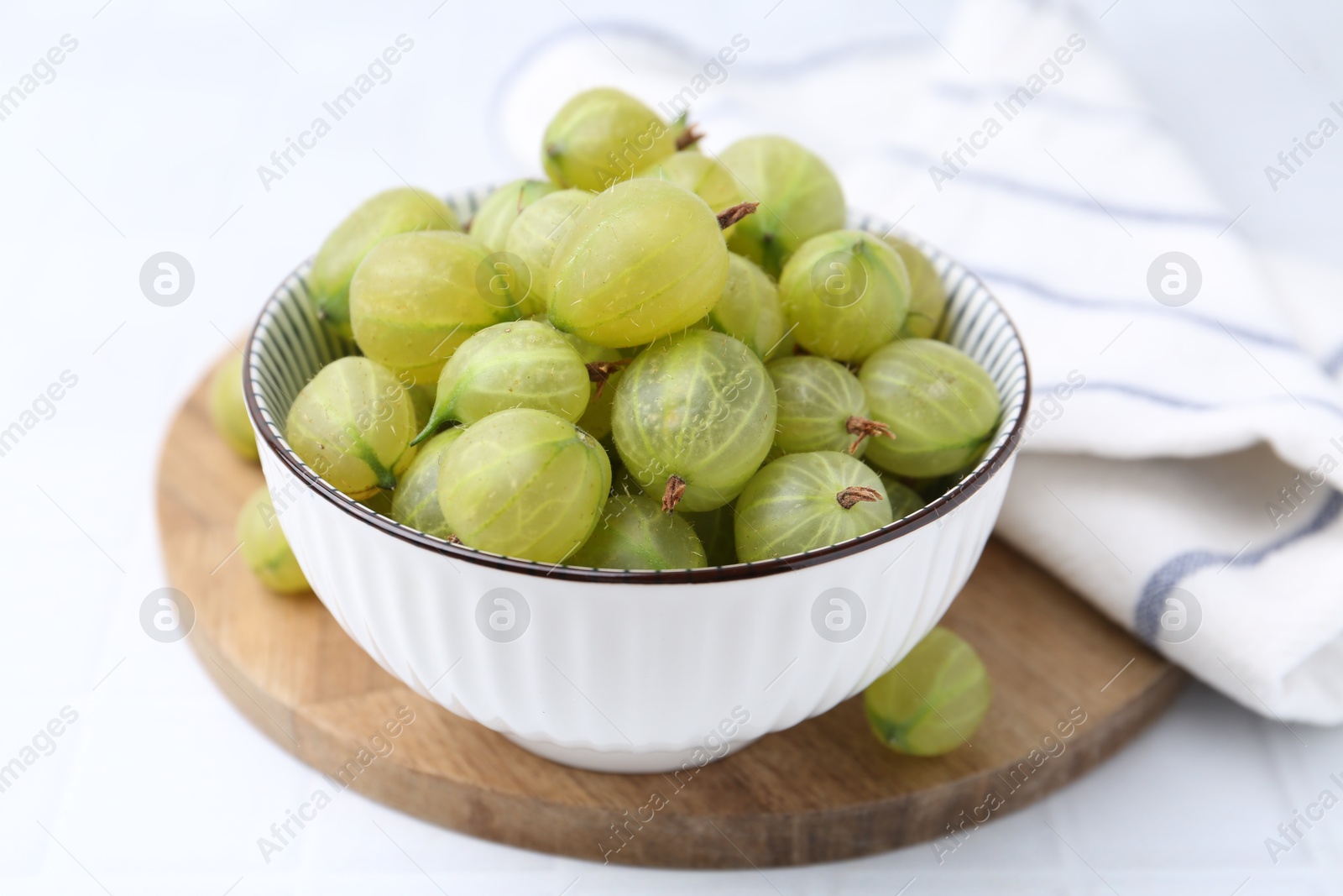 Fresh green gooseberries in bowl on white table, closeup Photo of Fresh green gooseberries in bowl on white table, closeup