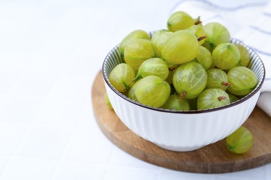 Photo of Fresh green gooseberries in bowl on white table, closeup. Space for text