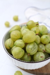 Photo of Fresh green gooseberries in bowl on white table, closeup