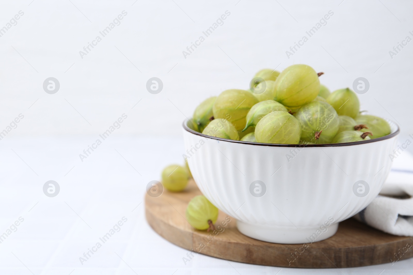 Fresh green gooseberries in bowl on white table, closeup. Space for text Photo of Fresh green gooseberries in bowl on white table, closeup. Space for text