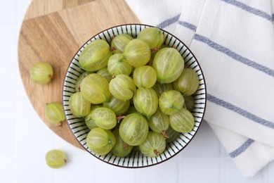 Photo of Fresh green gooseberries in bowl on white tiled table, top view