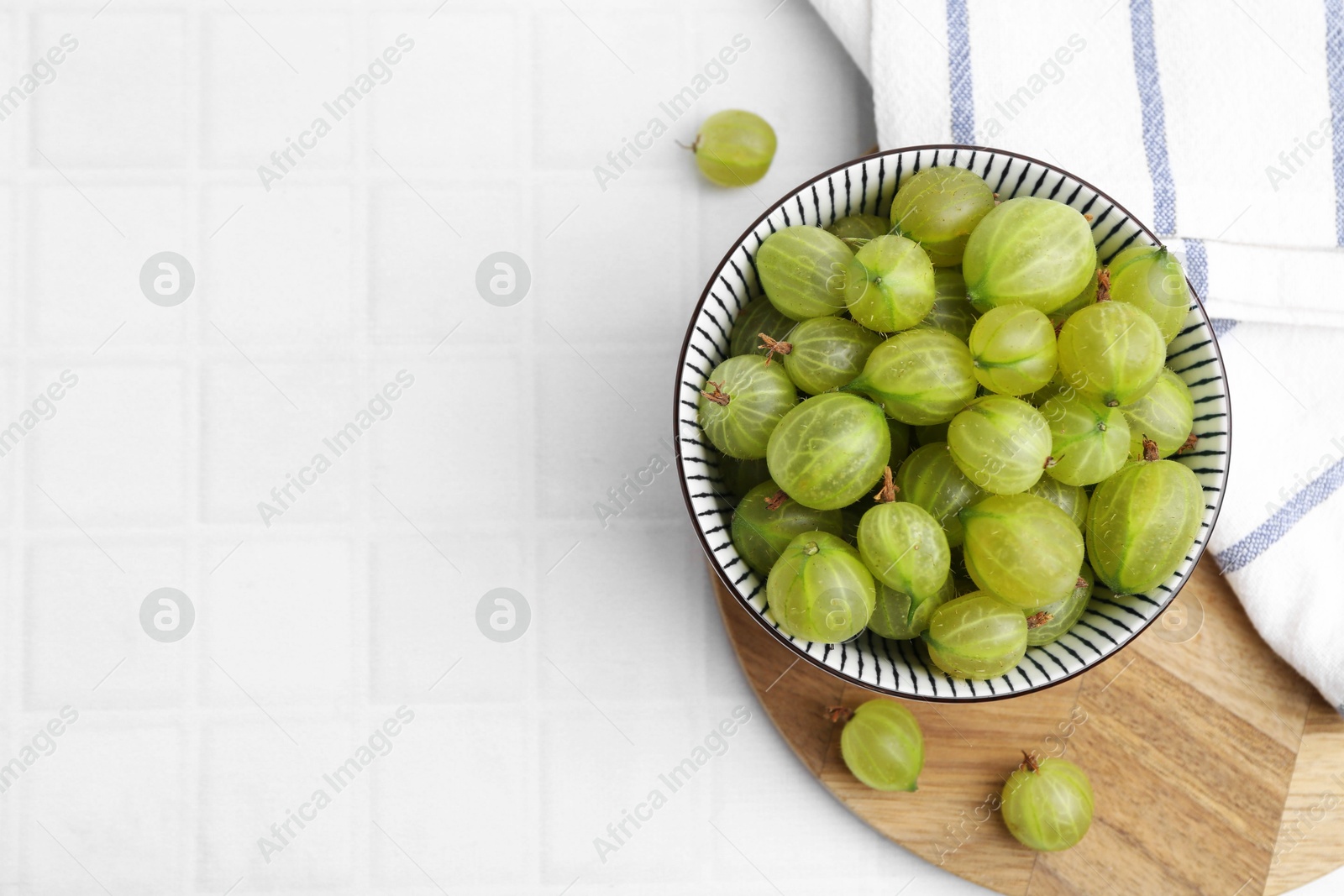 Fresh green gooseberries in bowl on white tiled table, top view. Space for text Photo of Fresh green gooseberries in bowl on white tiled table, top view. Space for text