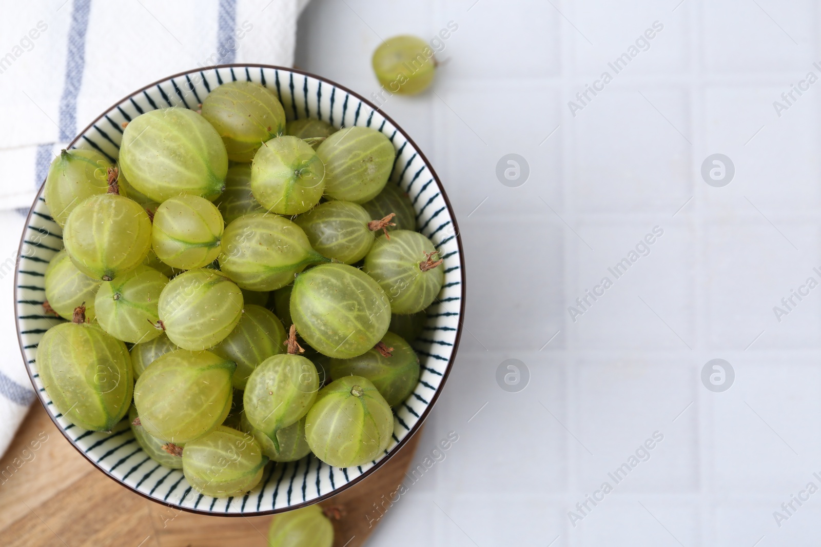 Fresh green gooseberries in bowl on white tiled table, top view. Space for text Photo of Fresh green gooseberries in bowl on white tiled table, top view. Space for text