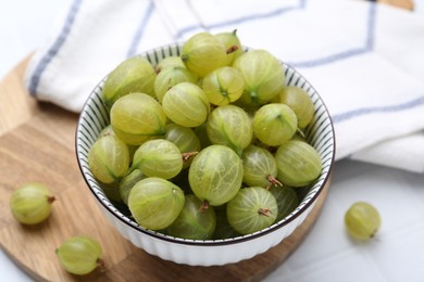 Photo of Fresh green gooseberries in bowl on white table, closeup