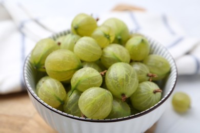 Photo of Fresh green gooseberries in bowl on white table, closeup