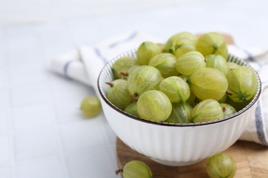 Photo of Fresh green gooseberries in bowl on white table, closeup