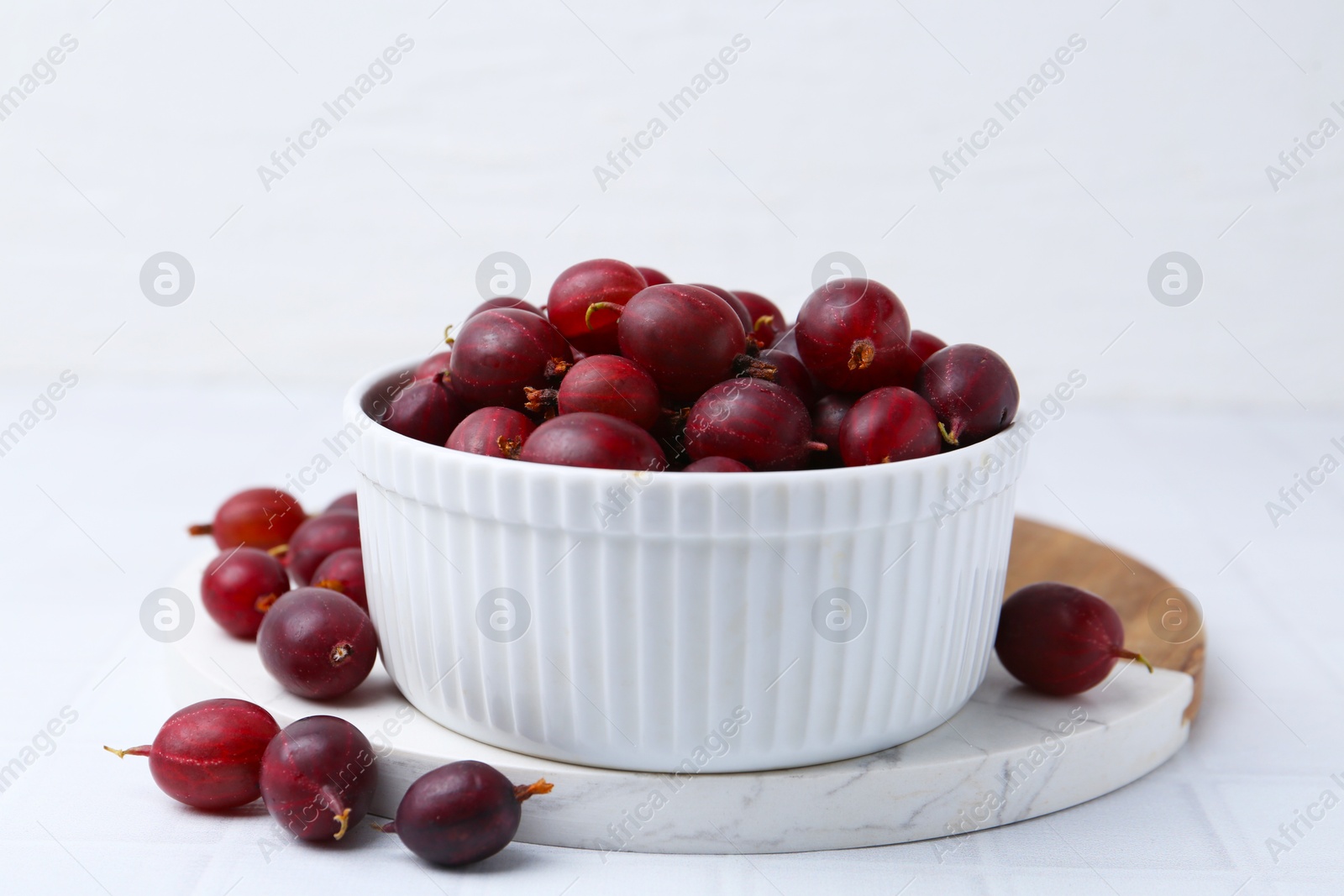 Ripe red gooseberries in bowl on white tiled table, closeup Photo of Ripe red gooseberries in bowl on white tiled table, closeup