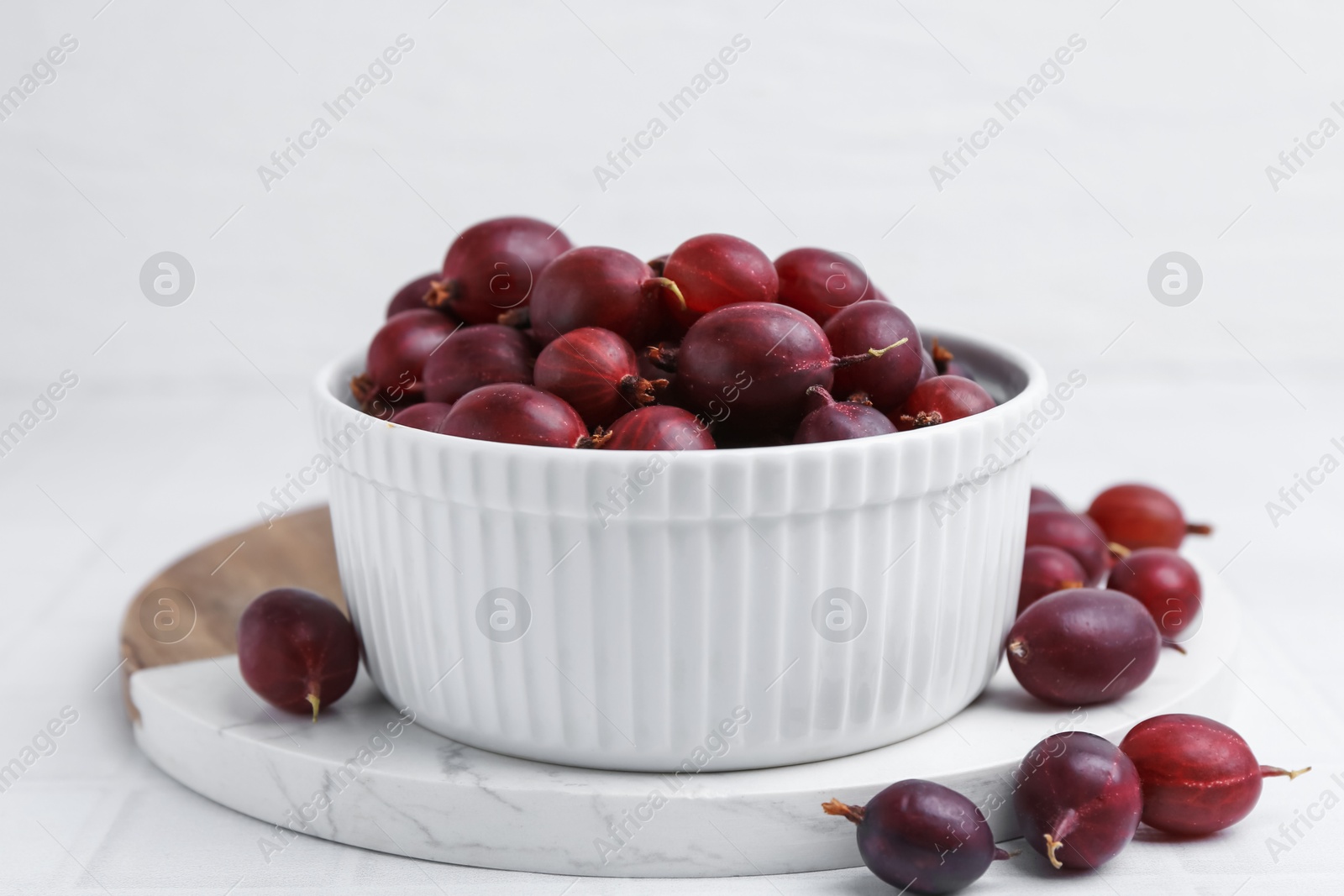 Ripe red gooseberries in bowl on white tiled table, closeup Photo of Ripe red gooseberries in bowl on white tiled table, closeup