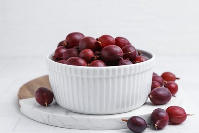 Photo of Ripe red gooseberries in bowl on white tiled table, closeup