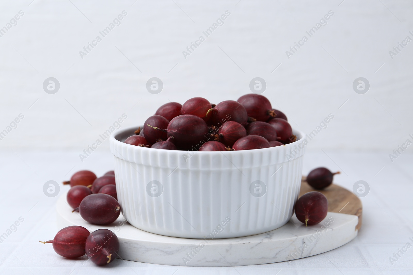 Ripe red gooseberries in bowl on white tiled table, closeup Photo of Ripe red gooseberries in bowl on white tiled table, closeup