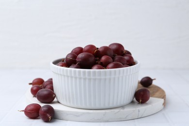 Photo of Ripe red gooseberries in bowl on white tiled table, closeup