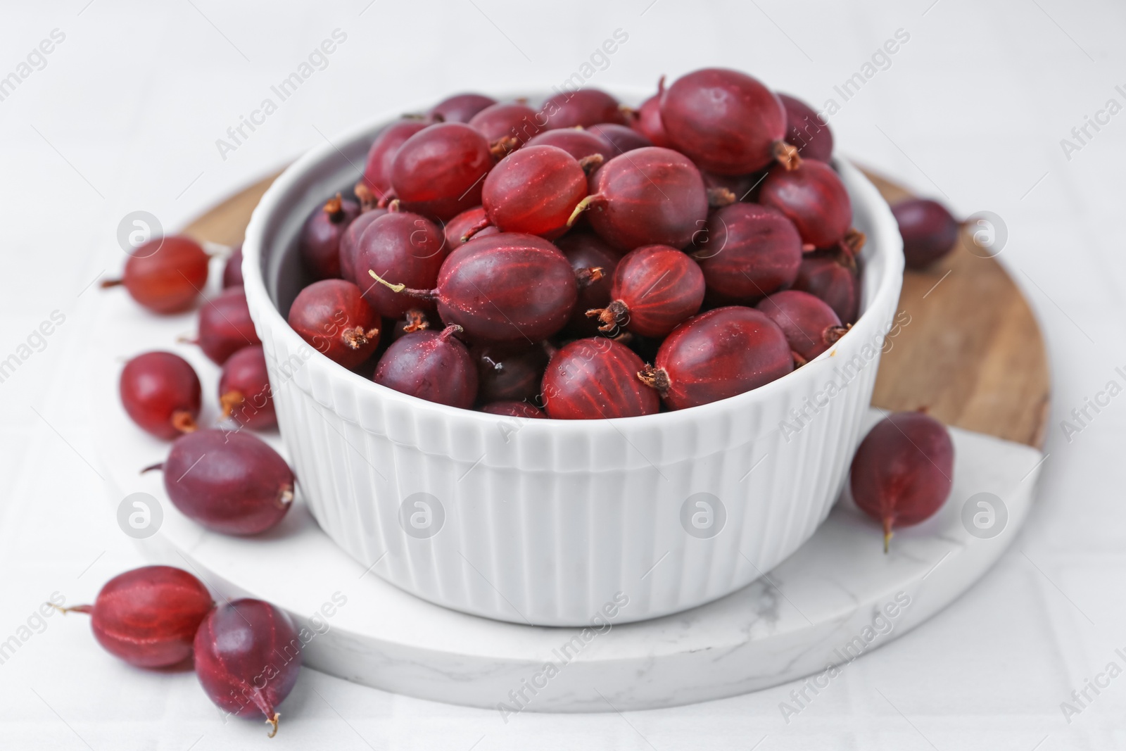 Ripe red gooseberries in bowl on white tiled table, closeup Photo of Ripe red gooseberries in bowl on white tiled table, closeup