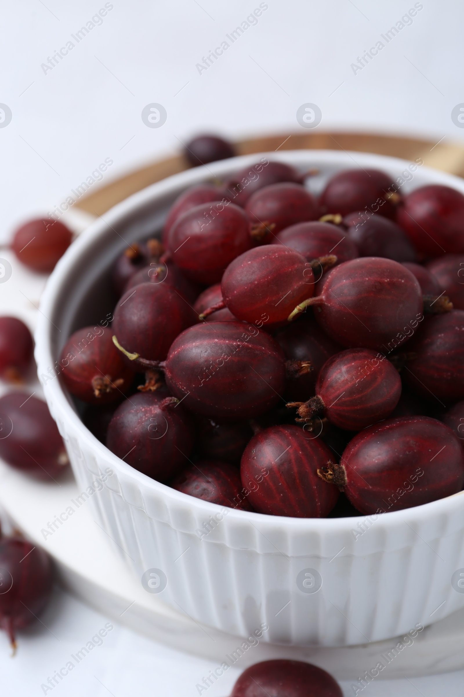 Ripe red gooseberries in bowl on white table, closeup Photo of Ripe red gooseberries in bowl on white table, closeup