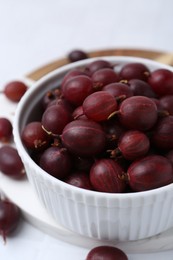 Photo of Ripe red gooseberries in bowl on white table, closeup