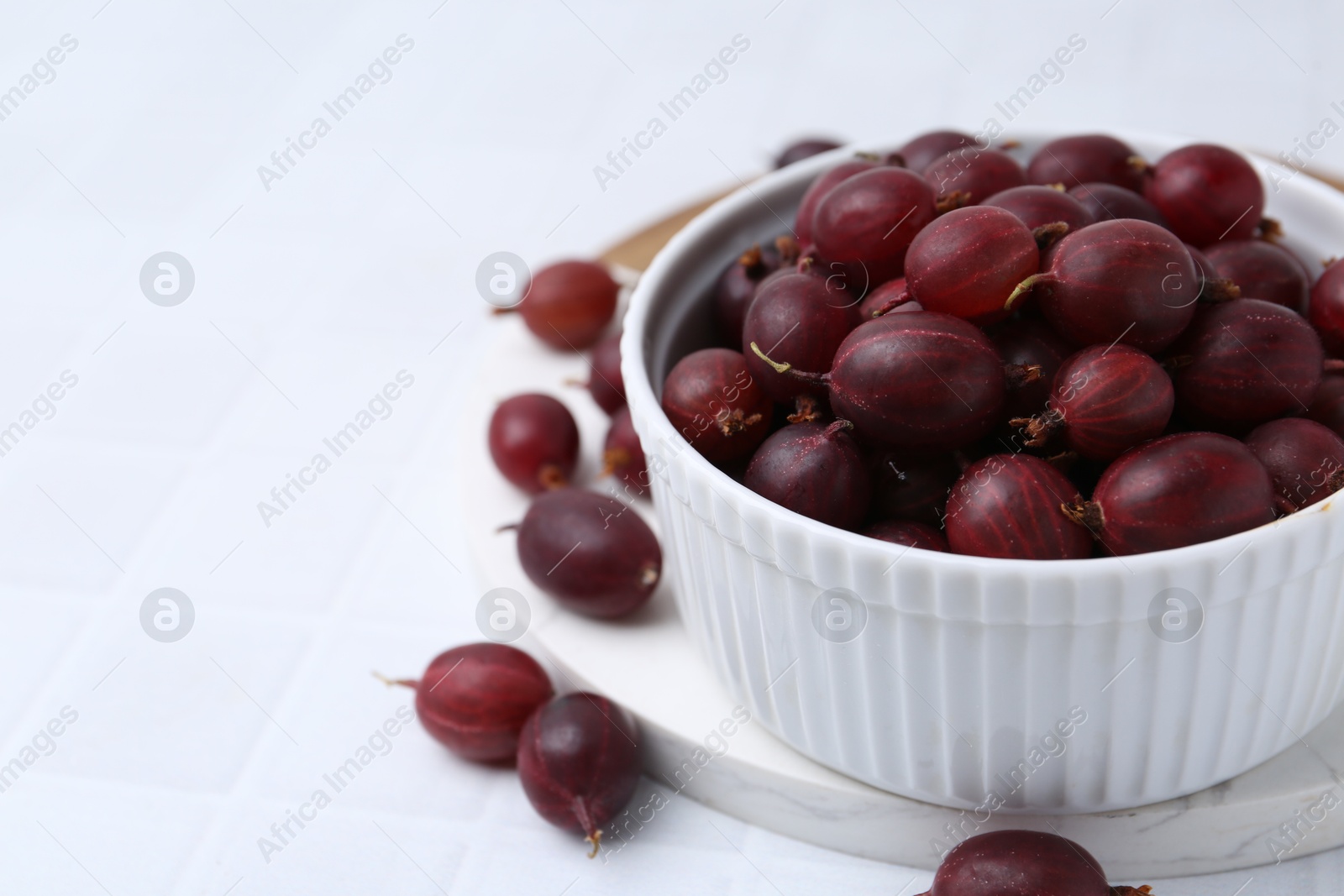 Ripe red gooseberries in bowl on white tiled table, closeup. Space for text Photo of Ripe red gooseberries in bowl on white tiled table, closeup. Space for text
