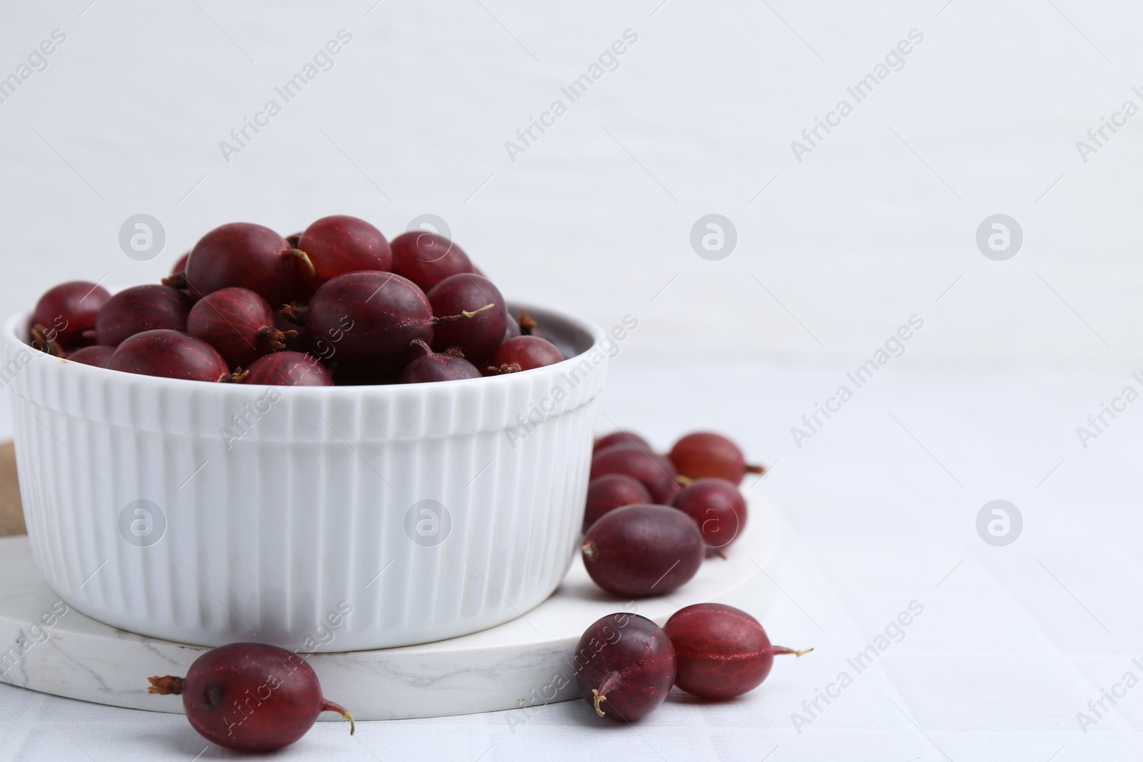 Ripe red gooseberries in bowl on white tiled table, closeup. Space for text Photo of Ripe red gooseberries in bowl on white tiled table, closeup. Space for text