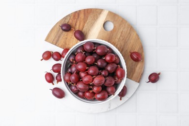Photo of Ripe red gooseberries in bowl on white tiled table, flat lay