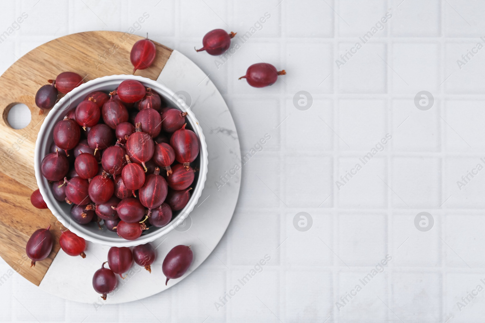 Ripe red gooseberries in bowl on white tiled table, flat lay. Space for text Photo of Ripe red gooseberries in bowl on white tiled table, flat lay. Space for text