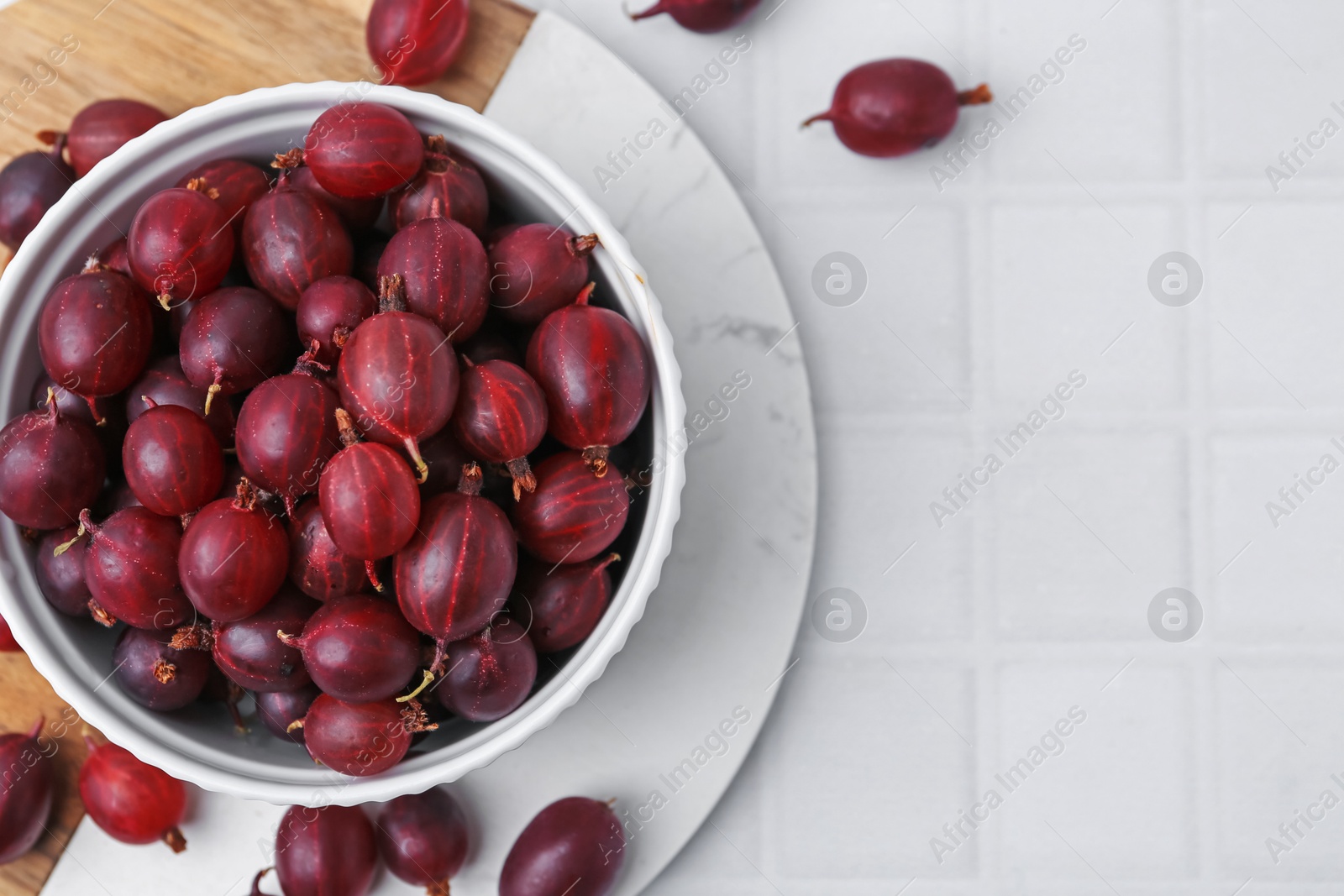 Ripe red gooseberries in bowl on white tiled table, flat lay. Space for text Photo of Ripe red gooseberries in bowl on white tiled table, flat lay. Space for text