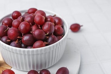 Photo of Ripe red gooseberries in bowl on white tiled table, closeup