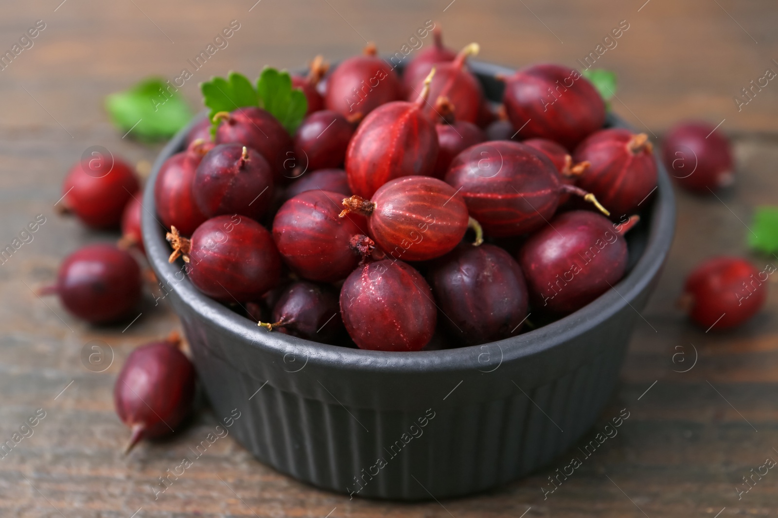 Ripe red gooseberries in bowl on wooden table, closeup Photo of Ripe red gooseberries in bowl on wooden table, closeup